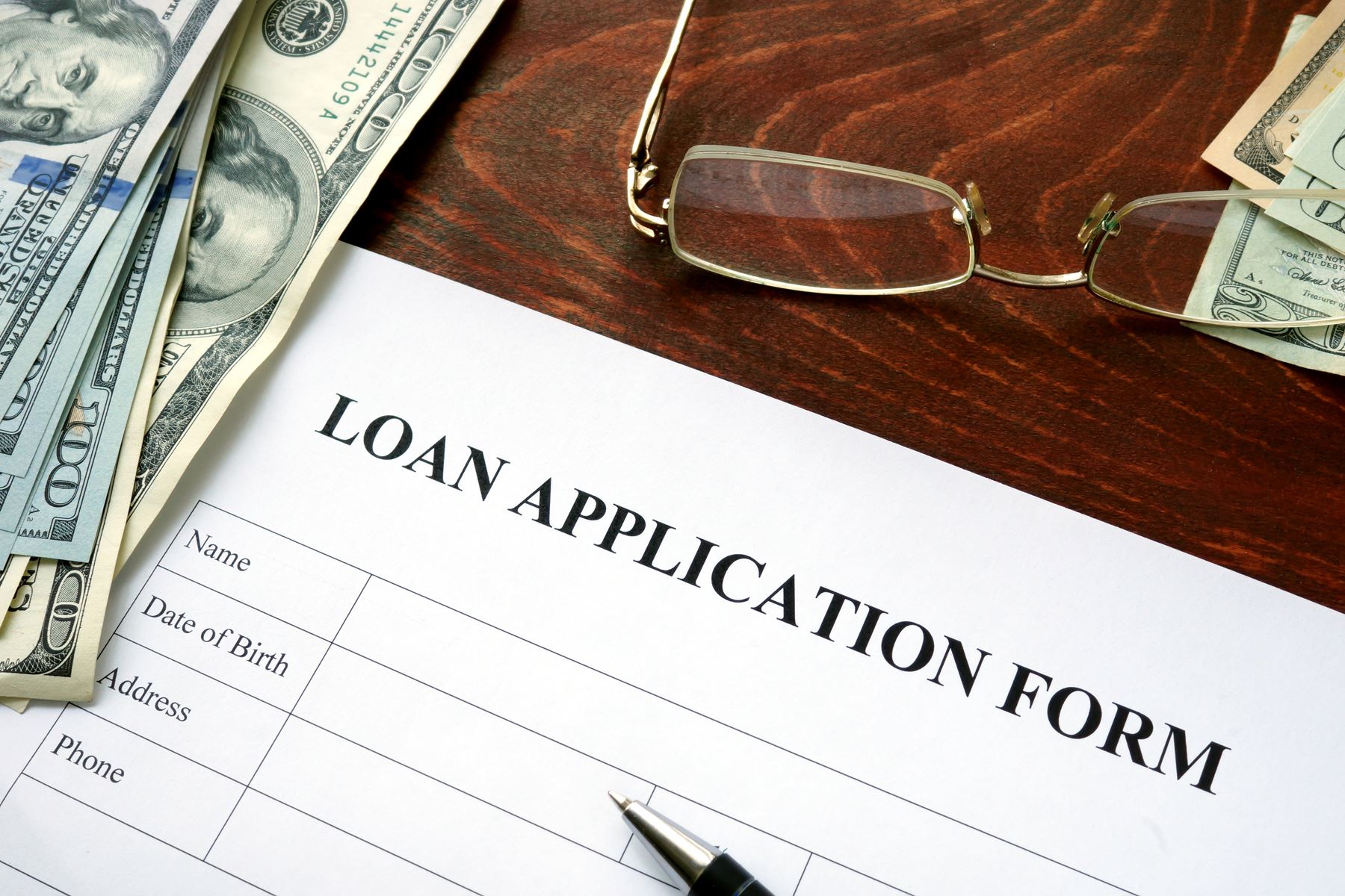 loan application, glasses and 100 dollar bill on a table