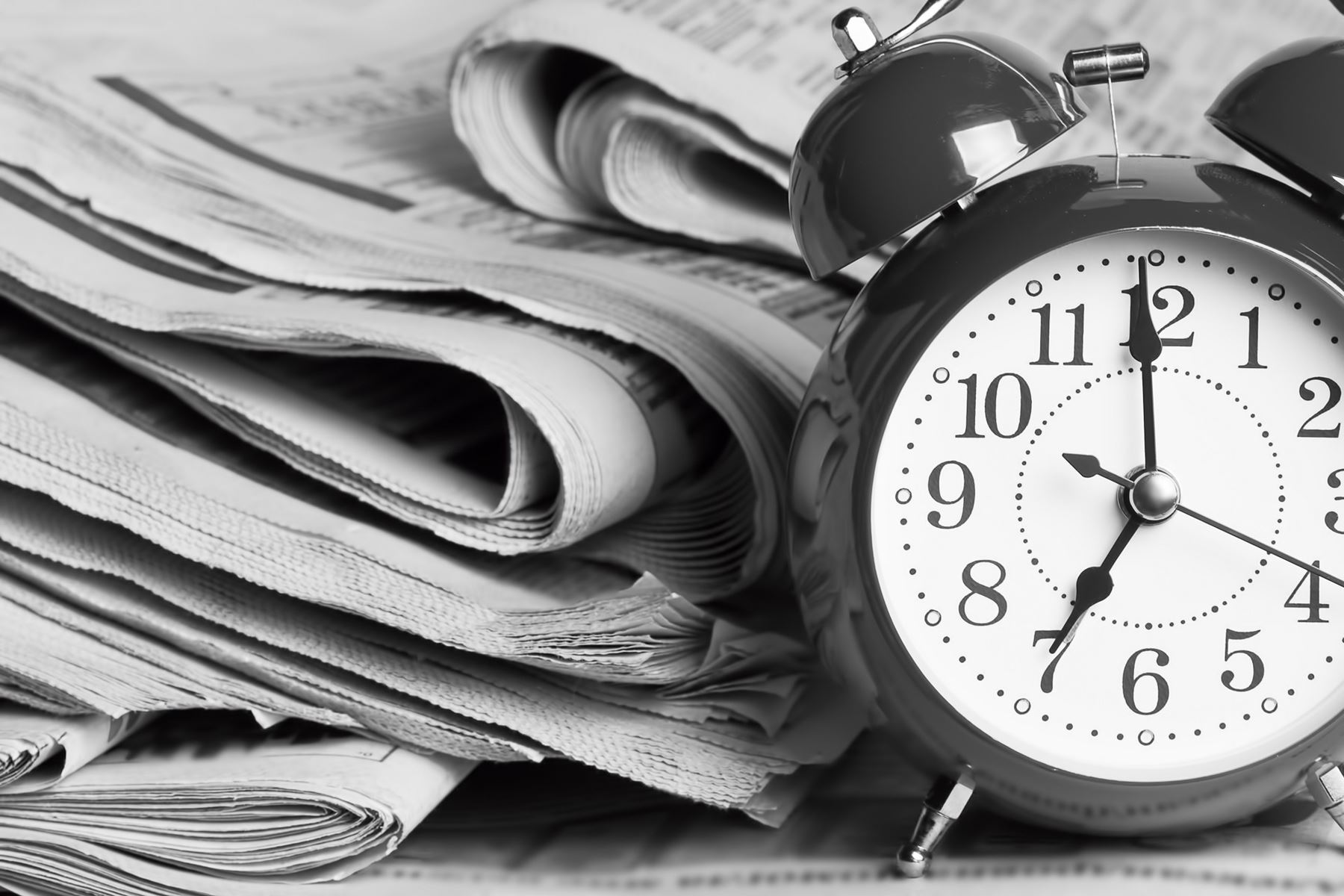 Alarm Clock sitting next to a stack of newspapers